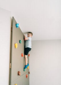 A young child climbs an indoor rock wall with colorful handholds during a gross motor activity.