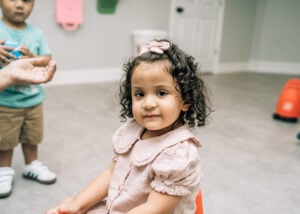 A young child sits on a foam block looking toward the camera during a structured play activity.