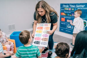A therapist shows a colors chart to children seated on the floor during a group learning activity.
