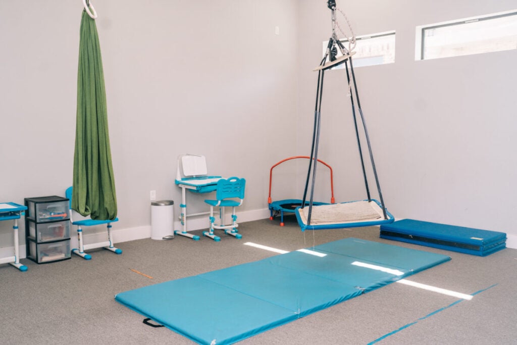 Occupational therapy sensory gym with swing, mats, and equipment for pediatric therapy.