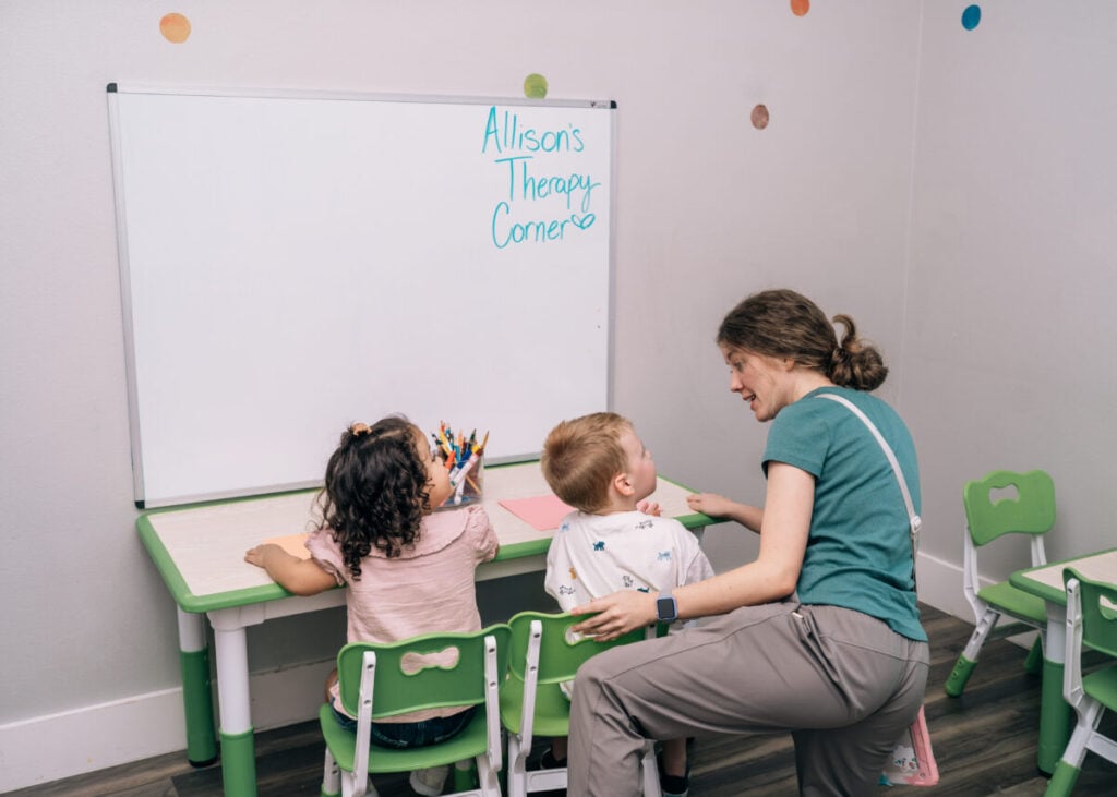 Therapist working with two children on communication and learning skills at table.
