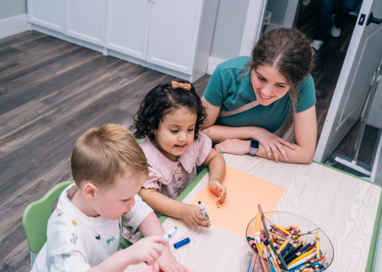 Therapist supporting children during table activity to build communication and fine motor skills.