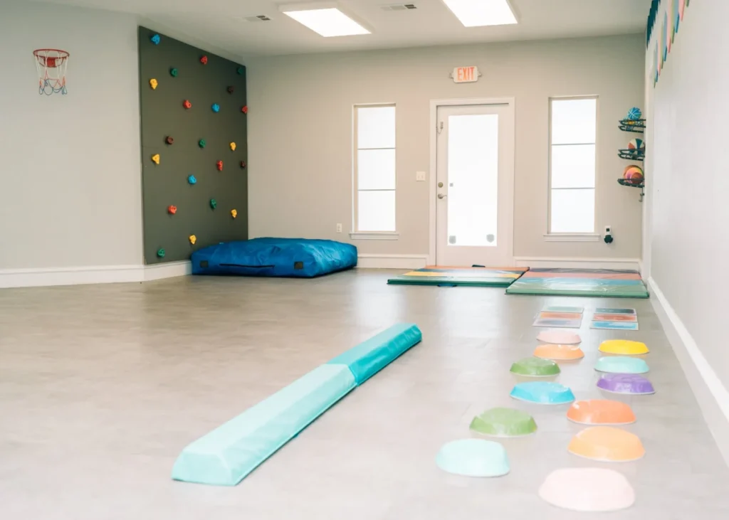 A spacious therapy gym with balance equipment, climbing wall, mats, and sensory path on the floor.