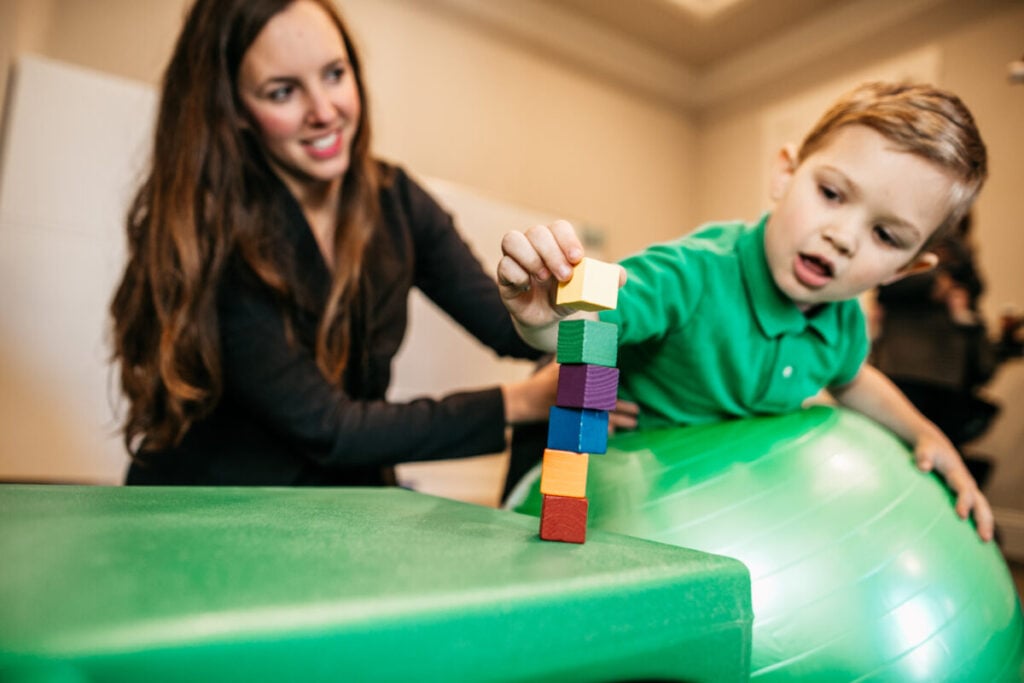 Child building fine motor skills stacking blocks during occupational therapy session.
