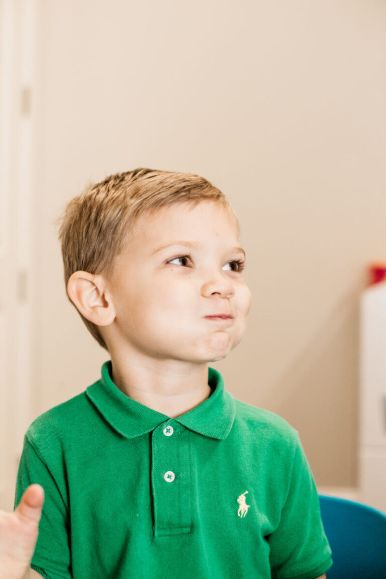 A young child with puffed cheeks looks to the side while practicing oral motor control.