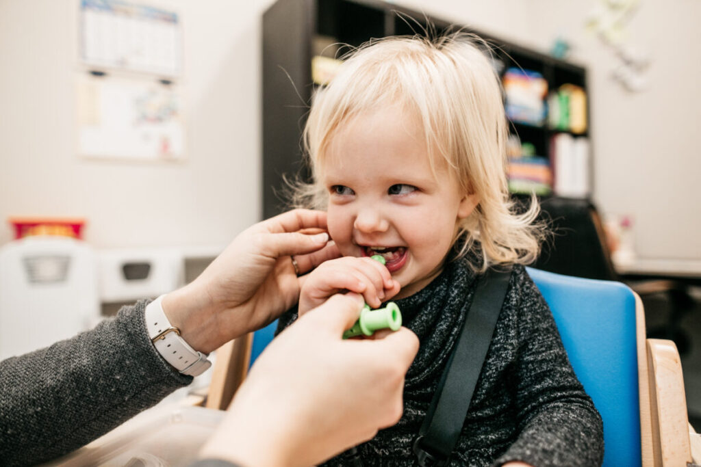 Toddler smiling during feeding therapy session with therapist support.