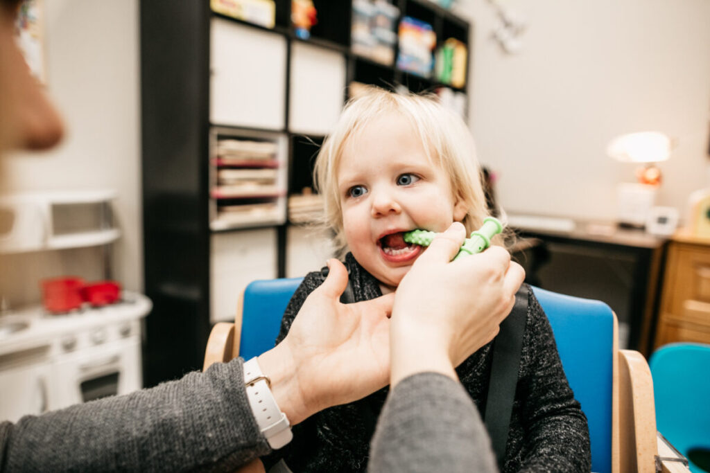 Therapist assisting toddler with oral motor feeding therapy in clinic setting.