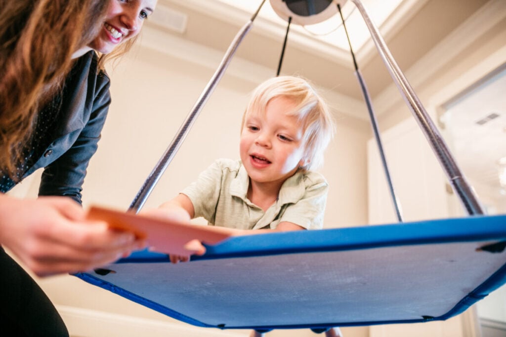 Child participating in sensory integration therapy using platform swing with therapist.
