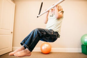 Child improving upper body strength with sensory swing activity in therapy clinic.