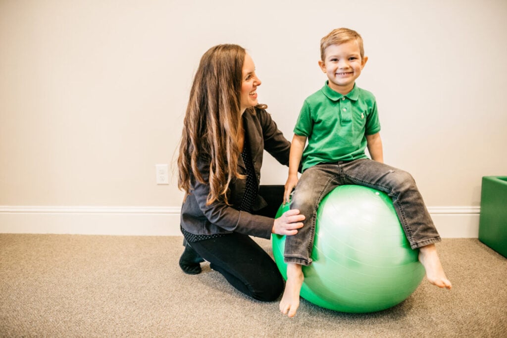 Child working on balance and core strength with occupational therapist using therapy ball.